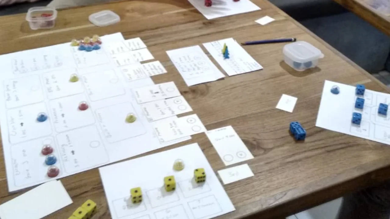 Handwritten paper game cards, dice, and colored tokens arranged for a tabletop playtest